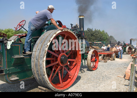 Man controlling steam traction engine used to drive a distant sawing bench working a large diameter belt driven saw blade Stock Photo