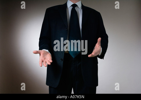 A man in a dark grey business suit gesturing with his hands as if making a point during a presentation Stock Photo