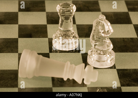 Glass Chess pieces on chessboard in checkmate Stock Photo