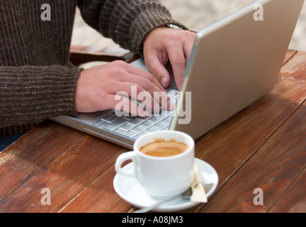 young man works on his laptop computer on coffetable in sidewalk cafe Stock Photo