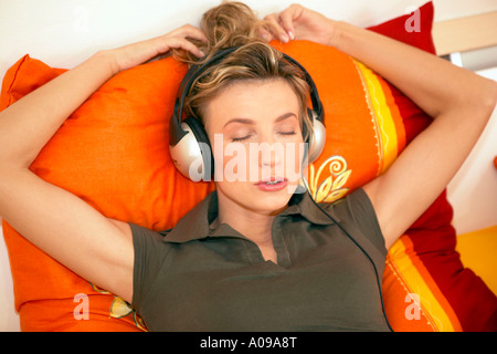 Frau liegt im Bett und hoert Musik, woman lying in bed and listening to music Stock Photo