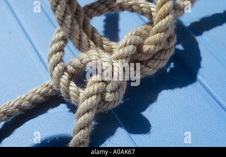 Thick clean rope tied in a complex knot and casting a shadow on a smooth blue surface Stock Photo