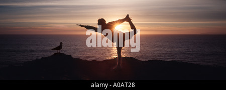 man in silhouette doing a yoga pose on the beach at sunset Stock Photo