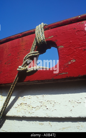 Detail of wooden boat with bright but peeling red and white paint tightly and neatly lashed down with rope under clear blue sky Stock Photo