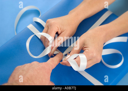 Close up of hands tying ribbon on gift Stock Photo