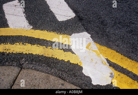 Detail of ragged-edged double yellow lines curving round a corner kerb and traversed by white Give Way lines Stock Photo