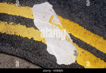 Detail of ragged-edged double yellow lines curving round a corner kerb and traversed  by white Give Way line Stock Photo