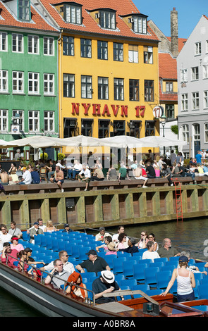 Sightseeing tour boat on Nyhavn canal and quayside cafe terraces, Copenhagen, Denmark Stock Photo