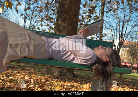 Young woman lying on park bench reading book autumn Stock Photo