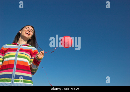 Young woman outdoors holding red balloon against blue sky low section view Stock Photo