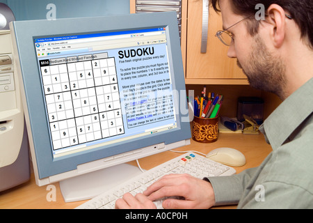 20's young man white playing Sudoku via internet on PC computer at home Stock Photo