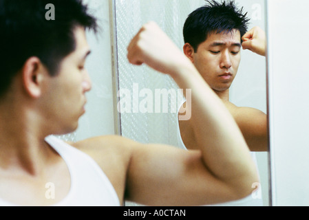 Disappointed young man flexing bicep in front of mirror Stock Photo