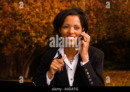 A 30 s African American executive does business on her cell phone and laptop outside in the back yard of her house Stock Photo