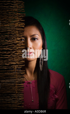Portrait of oriental woman Vietnamese American in traditional Vietnamese dress partially concealed behind wooden scrim Stock Photo