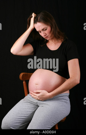 Young heavily pregnant woman holds unborn child baby foetus looking sad depressed anxious upset down baby blues third trimester Stock Photo