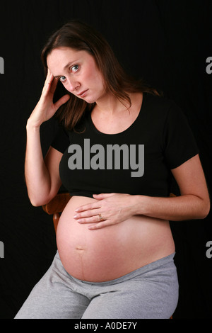 Heavily pregnant woman third trimester 34 weeks holds head on hands looking sad worried concerned upset depressed down unhappy Stock Photo