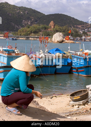 Vietnam Nha Trang city Cai River fishing harbour woman wearing traditional conical hat squatting on riverbank Stock Photo