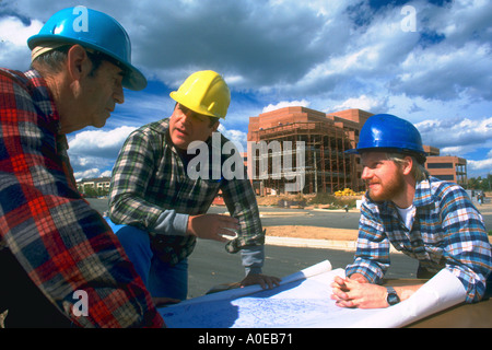 Two construction workers and their supervisor discuss plans for office building Stock Photo