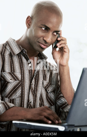 Man working on laptop computer while using mobile phone Stock Photo