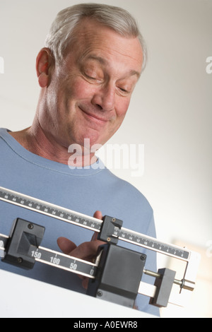 Happy mature man weighing himself whilst looking in mirror ...
