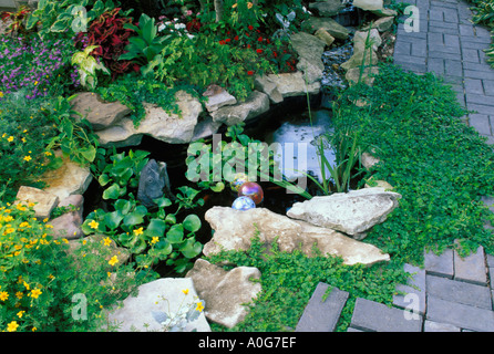 Small decorative fish pool with fountain waterfall in landscaped garden with brick paths and patio,  Midwest  USA Stock Photo