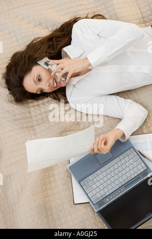 Businesswoman on mobile phone while lying on bed Stock Photo