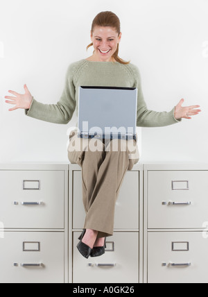 Woman with laptop atop file cabinets Stock Photo