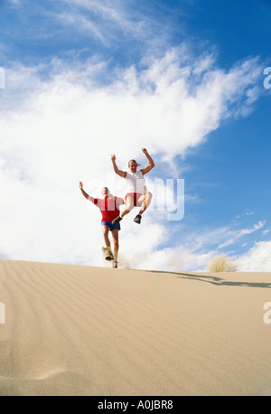 Two men leaping from sand dunes Stock Photo