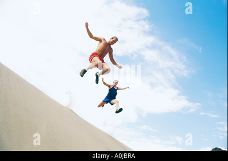 Two men leaping from sand dunes Stock Photo