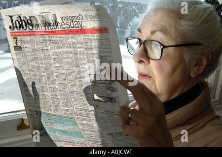 A thoughtful looking woman pensioner surveys the jobs on offer in her local paper. Stock Photo