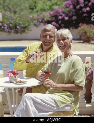 mature couple drinking wine by the poolside in summer sun Stock Photo