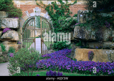 Gate in walled garden with blue pansies in border in Spring Stock Photo
