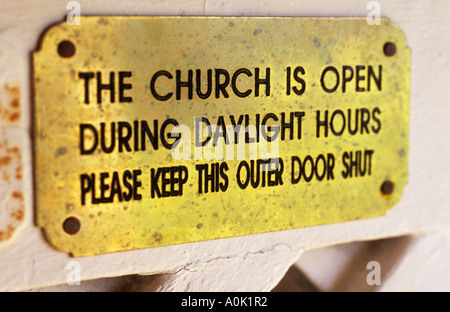 Close up of brass plate fixed to screen door stating The church is open during daylight hours Please keep this outer door shut Stock Photo