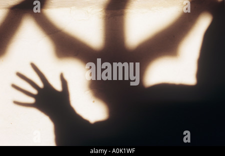 Shadow of a hooded monklike figure holding up his open hand in front of shadow of an ornate clear church window Stock Photo