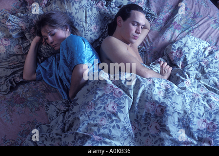 Unhappy Caucasian couple fighting in bed turning away from each other in bed Woman with tears in her eyes Stock Photo