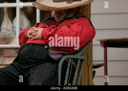 Cowboy in red shirt and sombrero sitting and sleeping on the boardwalk of an old town Stock Photo