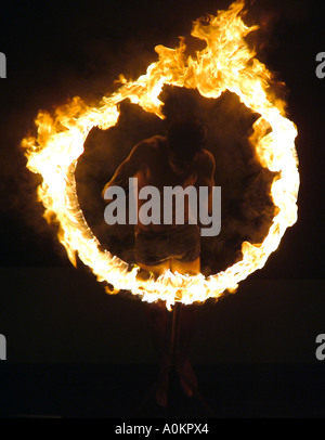 A ghostly image of a local Sri Lankan performer jumping through a blazing fire hoop in the darkness. Stock Photo