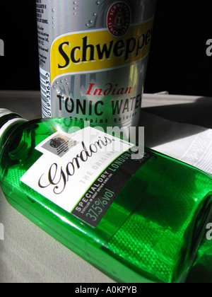 A miniture green Gordons gin bottle on its side with a can of tonic water in the background on an airplane seat table.