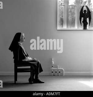 Nun sitting on chair in prayer. Stock Photo