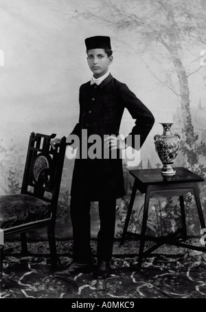 Old Historical Picture of one man dressed in old suit with pant standing with a chair India Stock Photo