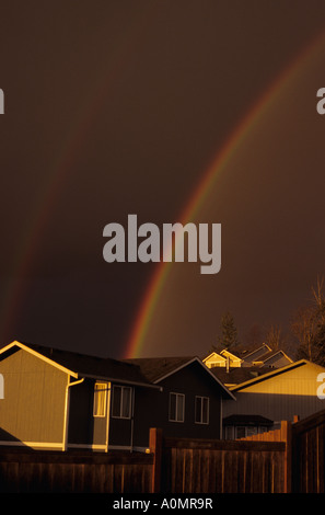 Dramatic light with sun breaking through stormy clouds to create a rainbow over homes in Marysville Washington State USA Stock Photo