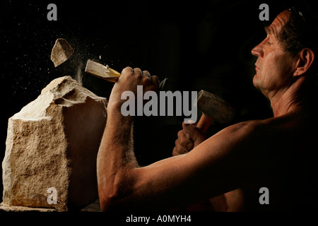 A stonemason works with hammer and cold chisel in studio light Stock Photo