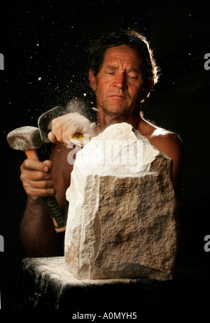 A stonemason works with hammer and cold chisel in studio light Stock Photo