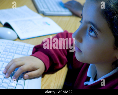 SCHOOL COMPUTER SCHOOLGIRL junior 5-7years Hispanic schoolgirl in uniform concentrating. at screen & keyboard in school computer classroom lessons Stock Photo