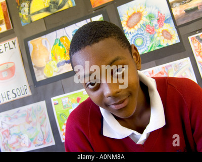 Schoolboy portait of a confident 13-15 years teenage black boy in school art classroom with his paintings on display in background Stock Photo