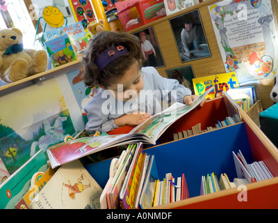 CHILD INFANT READING SCHOOL BOOKS CRÈCHE PRE-SCHOOL PLAY-SCHOOL Infant girl early-learning to read from books in kindergarten nursery school library Stock Photo