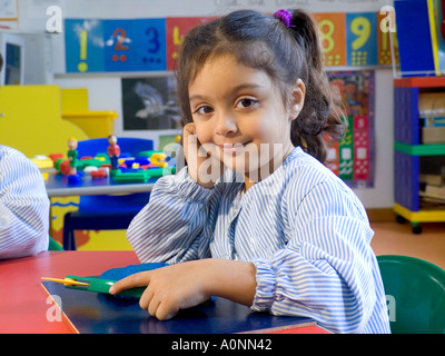 Infant girl three to five years at kindergarten table smiles to camera Stock Photo