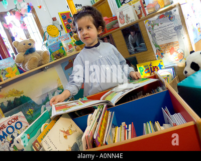 Young cute infant girl in play school learns to read from a selection of books in school kindergarten Stock Photo