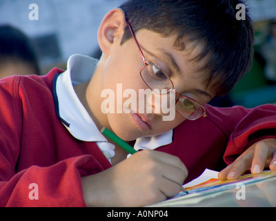 Junior schoolboy boy pupil 7-9 years wearing spectacles concentrating on his handwriting and art in school education learning classroom situation Stock Photo