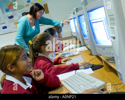 COMPUTER CLASS 1990’s Multicultural junior girl pupils in uniform & female teacher in modern school computer class room at computer screen terminals Stock Photo